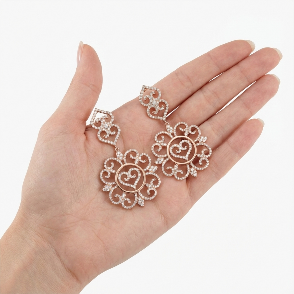hofjewellery Heartfall Éclat 18K rose gold earrings with 3.00ct round diamonds in an ornate heart design held in a hand.